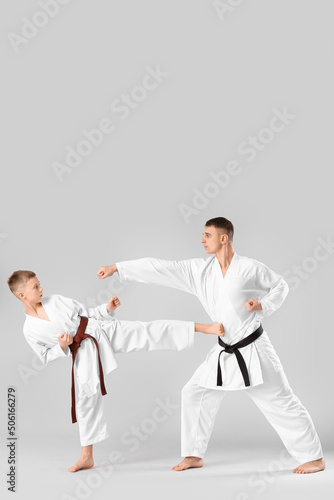 Boy practicing karate with instructor on light background