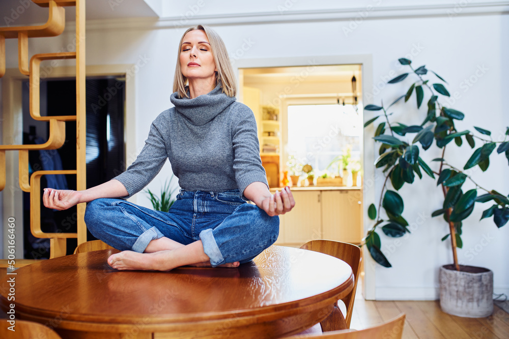 Mature woman meditating while sitting on a table at home Mature woman meditating while sitting on a table at home