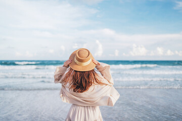 Summer beach vacation concept, Young woman with hat relaxing with her arms raised to her head enjoying looking view of beach ocean on hot summer day, copy space.