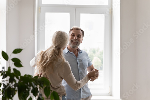 Happy cheerful retired couple celebrating marriage anniversary, family event at home, having fun at home, enjoying social dance activity to music, dating, party for two, talking, smiling © fizkes