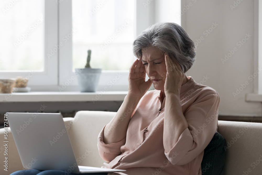 Stressed mature senior woman touching head with closed eyes at laptop computer, suffering from headache, migraine, blood pressure problem, health problems, feeling strong pain Stressed mature senior woman touching head with closed eyes at laptop computer, suffering from headache, migraine, blood pressure problem, health problems, feeling strong pain