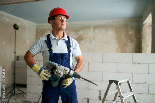 Tela Professional construction worker in uniform standing with rotary hammer drill