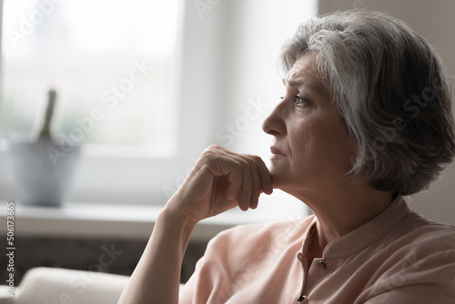 Frustrated sad mature grey haired 50s woman thinking over bad news, sitting on couch at home, feeling depressed, mourning, going through loss, grief, health problems, mental disorder, cancer disease