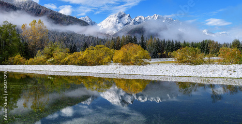 When autumn meets winter at the lake with perfect reflections in a calm water. Autumn trees with fresh snow and fog. 
