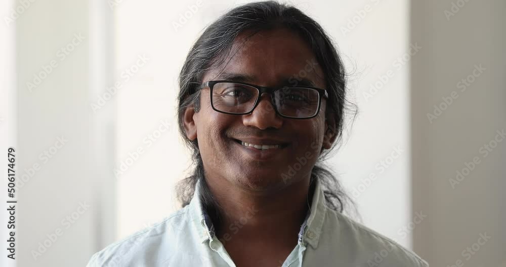 Headshot face portrait intelligent smiling long haired Indian male in eyeglasses worker teacher business owner corporate expert. Confident handsome businessman engineer pose in office look at camera Headshot face portrait intelligent smiling long haired Indian male in eyeglasses worker teacher business owner corporate expert. Confident handsome businessman engineer pose in office look at camera
