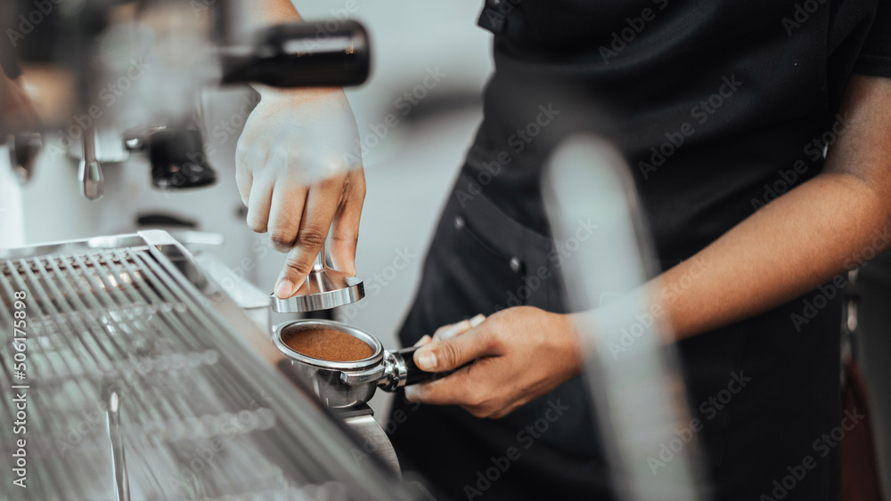 Barista using a tamper to press ground coffee into a portafilter. Close-up view on barista hands to making coffee with coffee machine. Coffee owner concept.