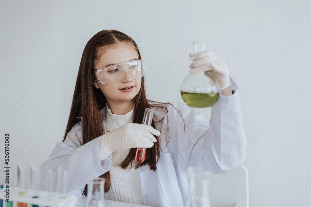 Caucasian girl student learning a chemical experiment in science class. Cute little girl holding test tube while learning chemistry class in white laboratory room. Caucasian girl student learning a chemical experiment in science class. Cute little girl holding test tube while learning chemistry class in white laboratory room.
