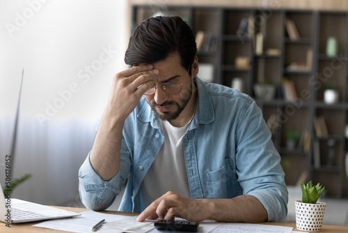 Financial problem. Concerned millennial businessman calculate taxes bills payments deal with debt bankruptcy overdue account. Worried young man accountant unable to form balance sheet look for mistake photo