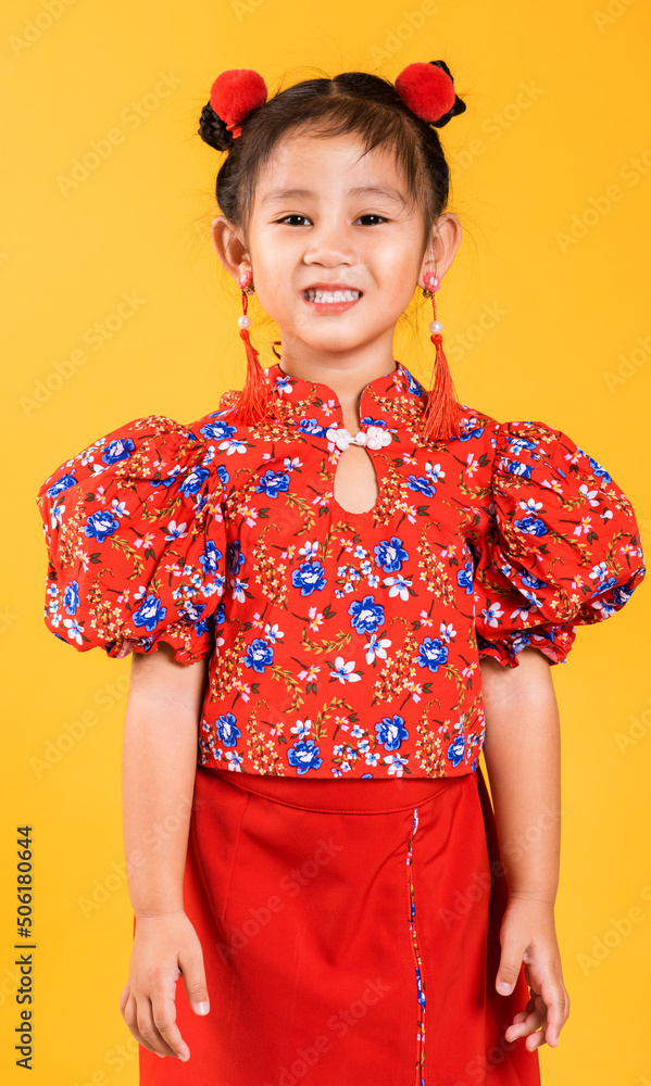 Happy Asian Chinese little girl smile wearing red cheongsam, Portrait children in traditional dress with greeting gesture celebration for Chinese New Year, studio short isolated on yellow background Happy Asian Chinese little girl smile wearing red cheongsam, Portrait children in traditional dress with greeting gesture celebration for Chinese New Year, studio short isolated on yellow background