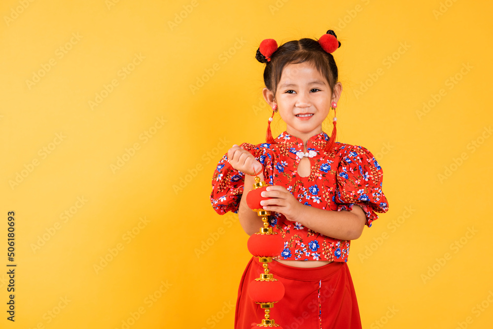 Chinese New Year. Happy Asian Chinese little girl smile wearing red cheongsam qipao holding silk lanterns on hand, Portrait children in traditional dress, studio short isolated on yellow background Chinese New Year. Happy Asian Chinese little girl smile wearing red cheongsam qipao holding silk lanterns on hand, Portrait children in traditional dress, studio short isolated on yellow background