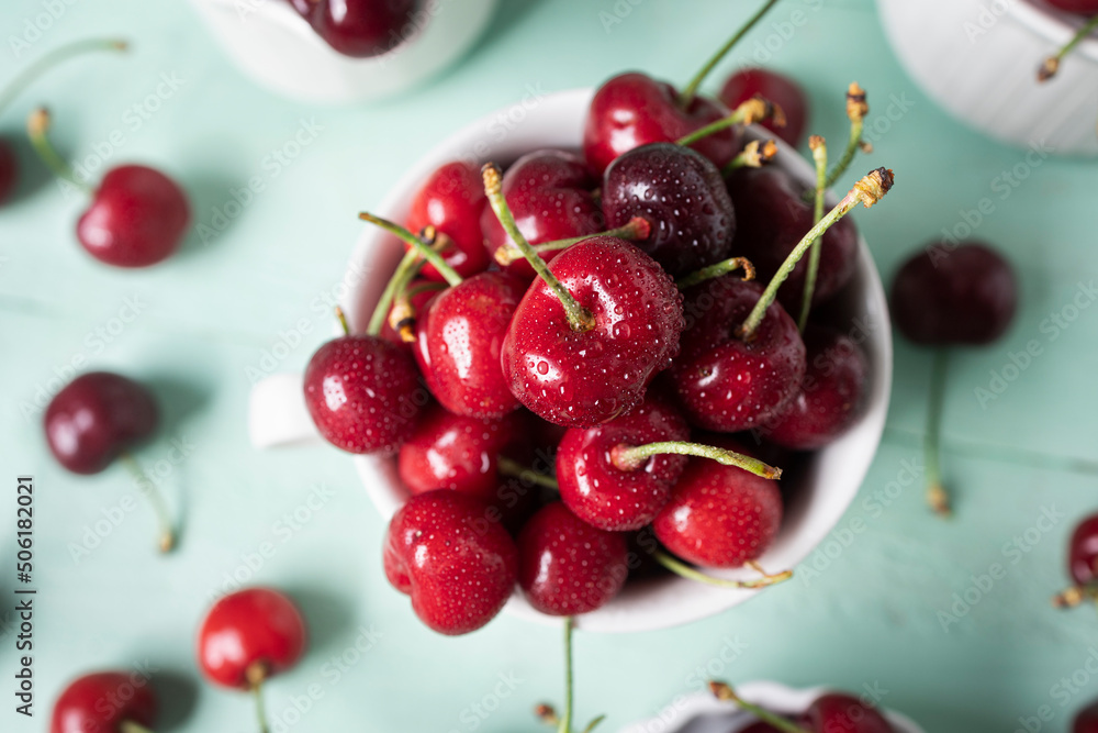 Delicious cherries in white ceramic cups on a light green wooden table Delicious cherries in white ceramic cups on a light green wooden table