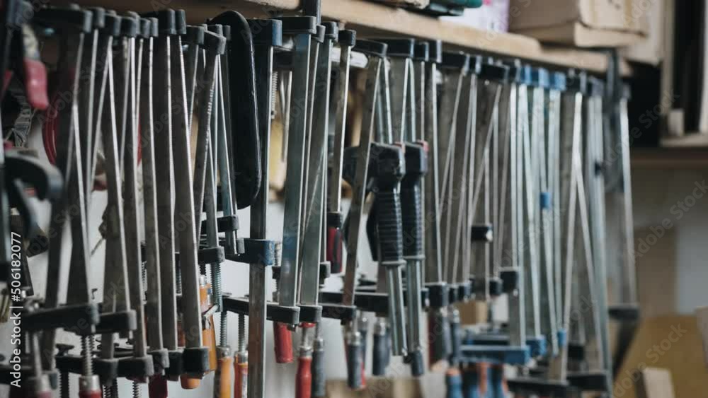 Many different clamps in the carpentry workshop. The tool hangs near the wall. Many different clamps in the carpentry workshop. The tool hangs near the wall.