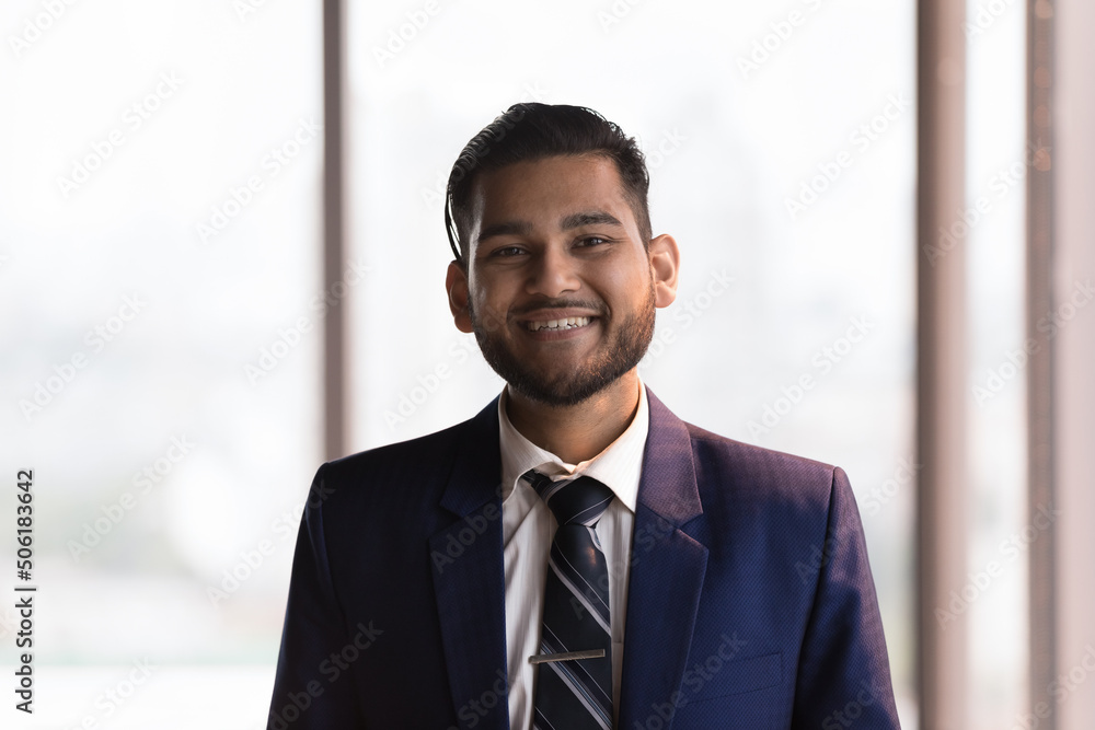 Head shot Indian businessman in formal suit pose in office smile staring at camera look proud by career growth, promotion, get hired in company position. Project leader, executive CEO portrait concept Head shot Indian businessman in formal suit pose in office smile staring at camera look proud by career growth, promotion, get hired in company position. Project leader, executive CEO portrait concept