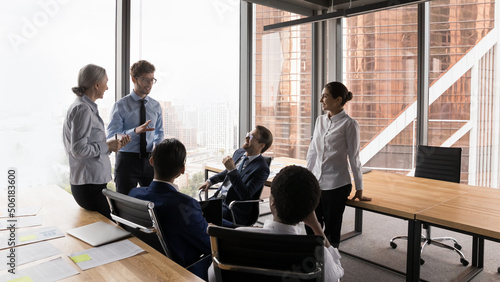 Six multi ethnic diverse business partners brainstorming, think over collaborative task, share opinion, listen to team leader, take part at group meeting in modern city office. Briefing event concept