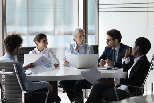 Diverse corporate staff discuss report shown in charts and graphs, analyzing financial stats, do paperwork involved in project analysis during meeting in boardroom. Brainstorming, negotiations concept photo