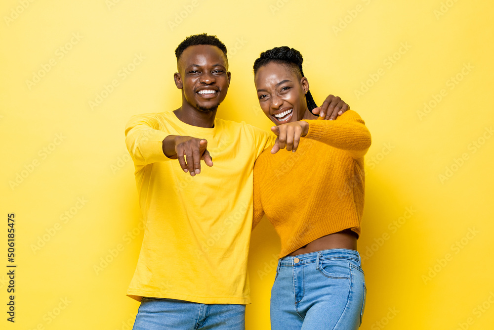 Happy African couple holding each other and pointing hands at you in yellow color studio isolated background Happy African couple holding each other and pointing hands at you in yellow color studio isolated background