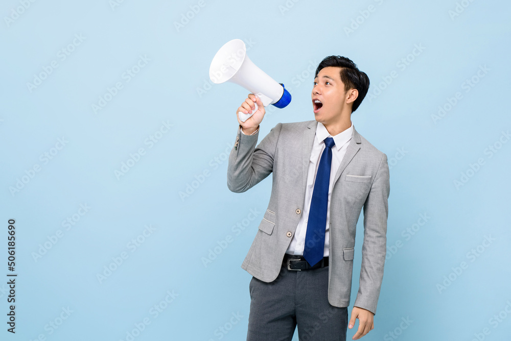 Young handsome Asian man in formal business suit holding megaphone and yelling in isolated light blue color studio background Young handsome Asian man in formal business suit holding megaphone and yelling in isolated light blue color studio background