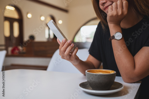 Closeup image of a young asian woman holding and using mobile phone with coffee cup on the table