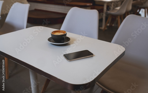 A single mobile phone and coffee cup on the table in cafe