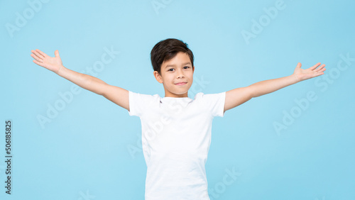 Cute smiling handsome mixed race boy with open arms in isolated light blue color studio background