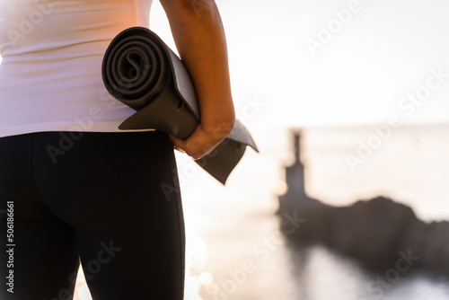 Hands of a woman with the yoga mat in nature by the sea, healthy and naturist life, outdoor pilates