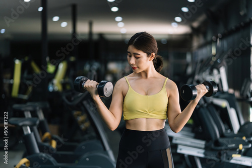 Beautiful young Asian woman doing exercises in gym to stay fit. Fit female exercising with dumbbell weights. © amnaj