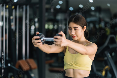 Beautiful young Asian woman doing exercises in gym to stay fit. Fit female exercising with dumbbell weights.