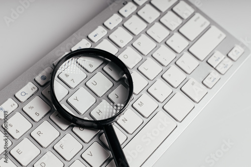 Close-up image with magnifying glass on a keyboard on a white background. Internet search concept