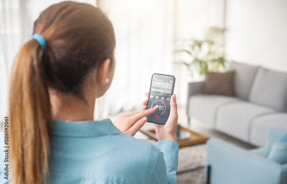 Woman controlling the thermostat using her smartphone Woman controlling the thermostat using her smartphone