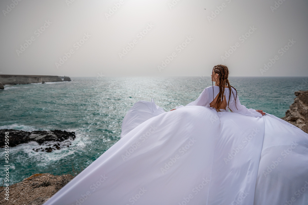 Happy freedom woman on the beach enjoying and posing in white dress. Rear view of a girl in a fluttering white dress in the wind. Holidays, holidays at sea. Happy freedom woman on the beach enjoying and posing in white dress. Rear view of a girl in a fluttering white dress in the wind. Holidays, holidays at sea.
