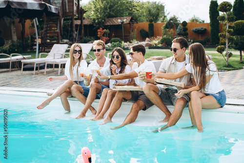 Group of young people having fun at backyard poolside party, enjoying sunny summer days outdoor, drinking cocktails and eating pizza and sushi..
