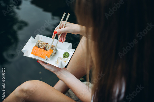 Girl eating sushi sitting near a pond with carp