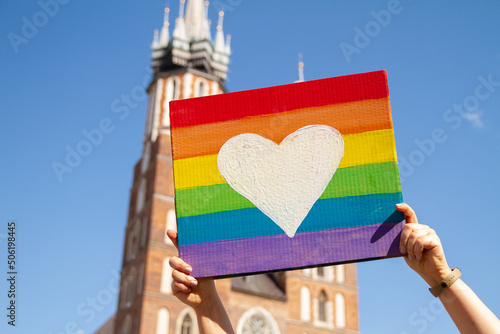 Rainbow heart placard sign, symbol of LGBT love. Pride Parade equality march in Krakow, Poland to support and celebrate LGBT+, LGBTQ. Saint Mary's Basilica (Mariacki Church Kraków) in background. © Longfin Media