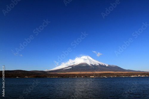 Fuji mountain with snow and fog covered top  lake or sea and clear blue sky background with copy space. This place famous in Japan and Asia for people travel to visit and take picture.