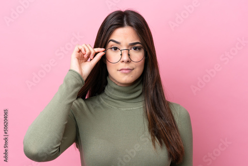 Young Brazilian woman isolated on pink background With glasses and frustrated expression