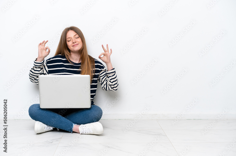 Young caucasian woman with a laptop sitting on the floor isolated on white background in zen pose Young caucasian woman with a laptop sitting on the floor isolated on white background in zen pose
