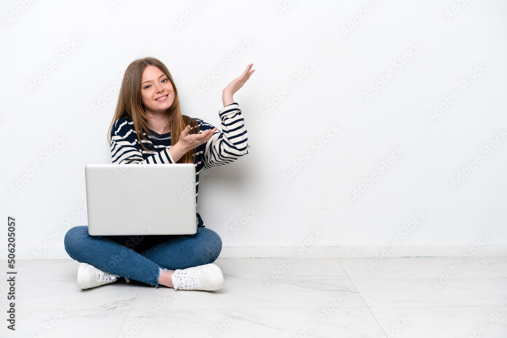Young caucasian woman with a laptop sitting on the floor isolated on white background extending hands to the side for inviting to come Young caucasian woman with a laptop sitting on the floor isolated on white background extending hands to the side for inviting to come