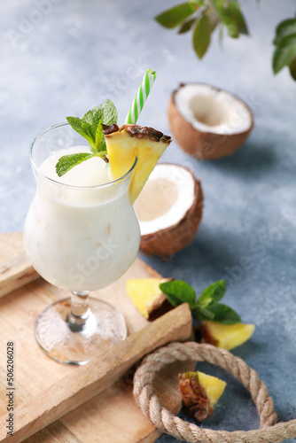 Summer. Drinks and cocktails. Pina colada in glass with pineapple, coconut, mint and a branch of greenery on a light gray background. Background image, copy space