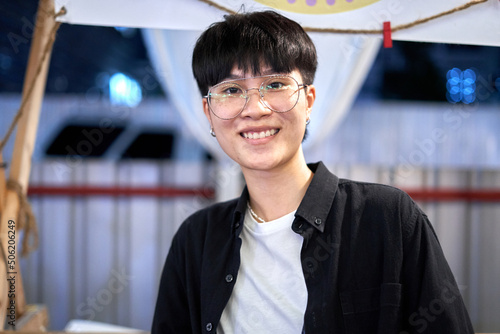 Portrait of a non binary person in casual clothes and glasses in a night market photo