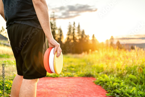 Disc golf in summer at sunset. Man with frisbee equipment in park course. Guy playing discgolf. Player in outdoor sport tournament. Landscape in Finland.