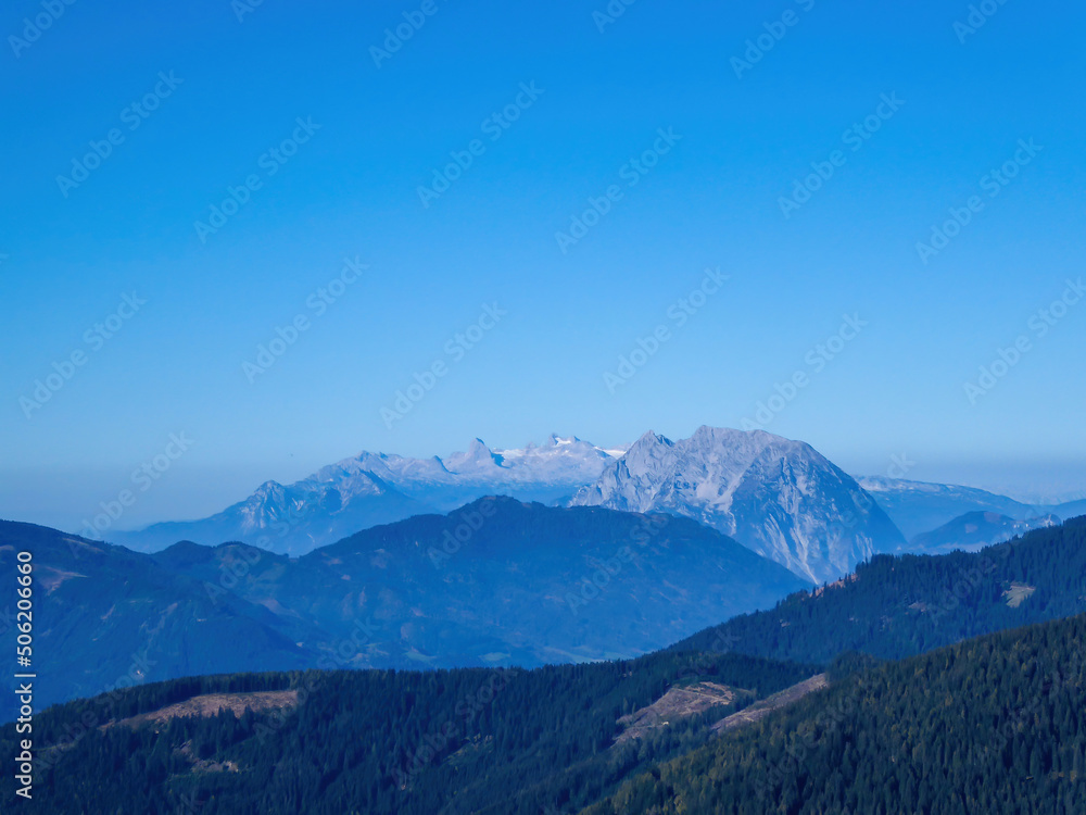 A panoramic view on a massive, stony Alps from Kaiserau Kreuzkogel region in Austria. There are endless mountains chains in the back. The slopes are overgrown with moss and grass. Sunny and bright day