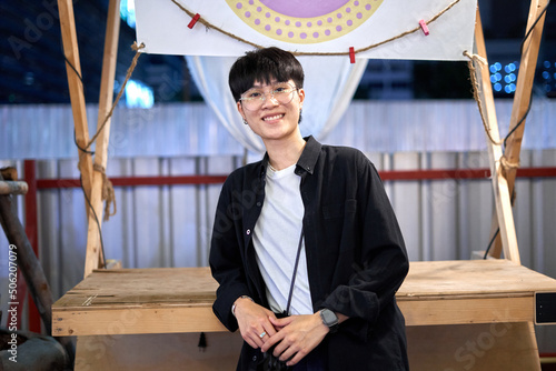 Portrait of a non-binary person smiling to the camera in an urban night fair