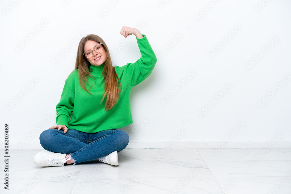 Young caucasian woman sitting on the floor isolated on white background doing strong gesture Young caucasian woman sitting on the floor isolated on white background doing strong gesture