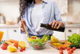 Lady cooking fresh vegetable salad, adding olive oil and seasoning to bowl, enjoying eating healthy vegetarian food