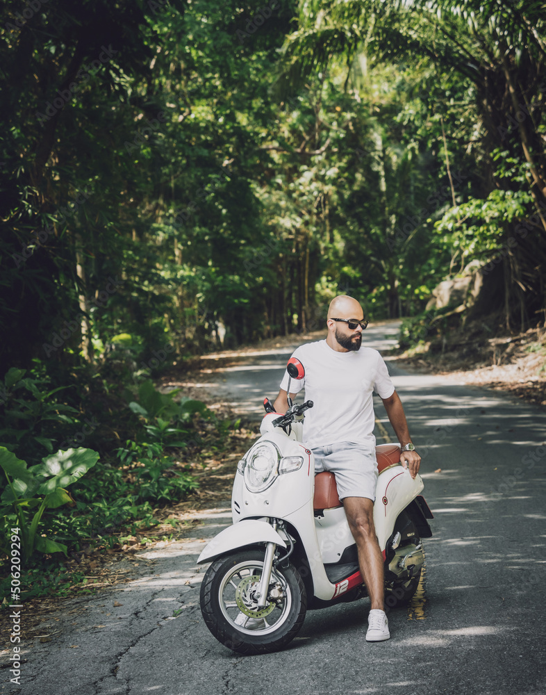 Stylish young man and his motorbike on the road in the jungle Stylish young man and his motorbike on the road in the jungle