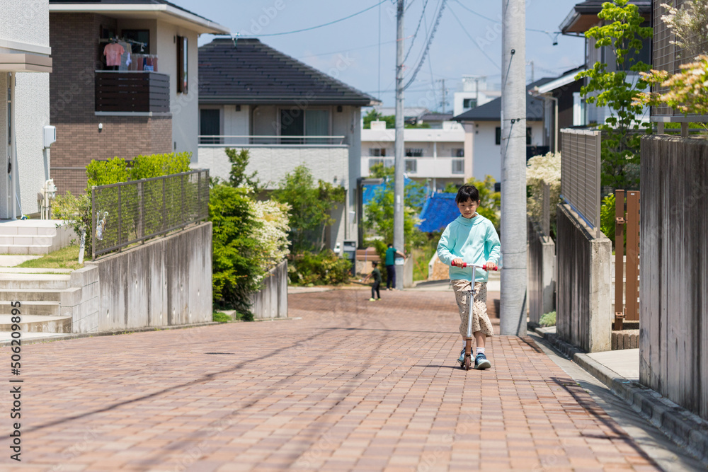 夏の名古屋の住宅地でスクーターを遊んでいる可愛い小学生の女の子の姿