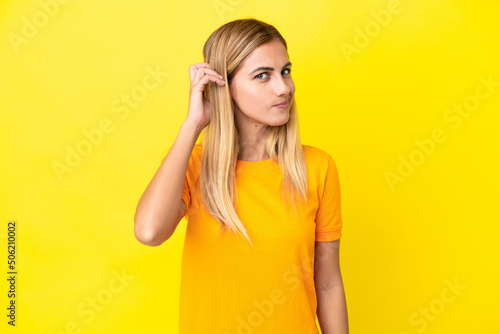 Blonde Uruguayan girl isolated on yellow background having doubts