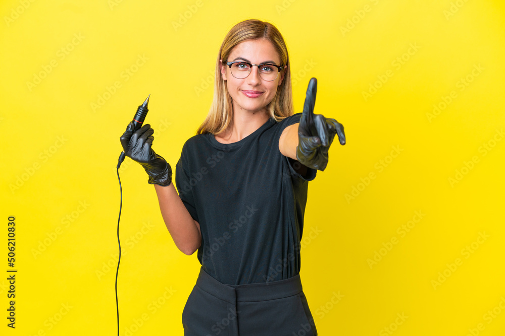 Tattoo artist Uruguayan woman isolated on yellow background showing and lifting a finger Tattoo artist Uruguayan woman isolated on yellow background showing and lifting a finger