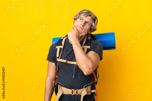 Young mountaineer man over isolated yellow background having doubts