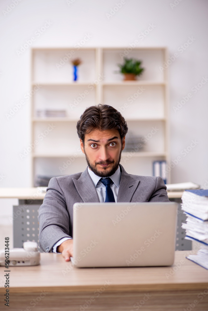 Young male employee and too much work in the office Young male employee and too much work in the office